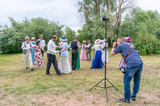 De fotograaf maakt foto's van dansende mensen in vintage kostuums, in de natuur