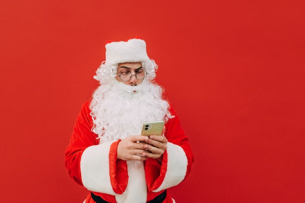 De geconcentreerde Kerstman fronst zijn wenkbrauwen bij het gebruik van een smartphone