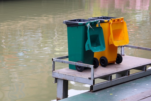 De gele en groene afvalbak dichtbij de rivier in thailand