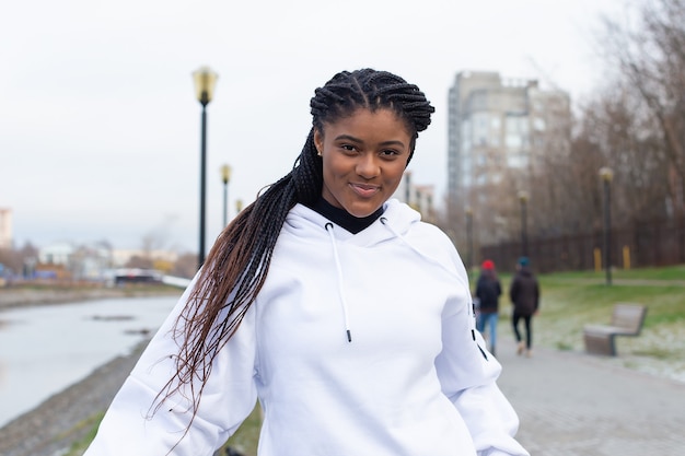 De gelukkige Afro-Amerikaanse vrouw in een park in een witte hoodie