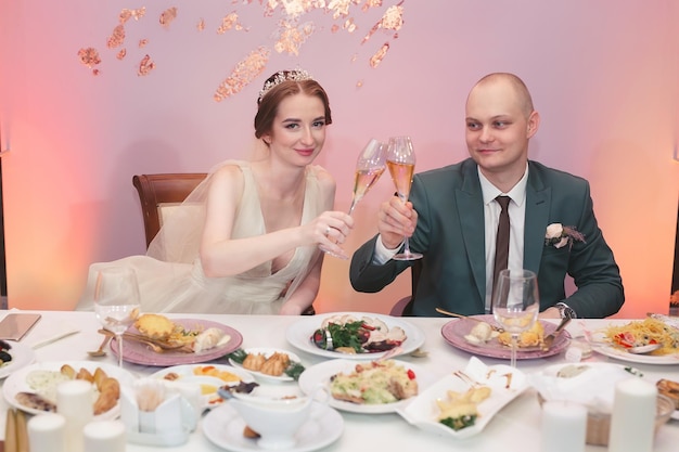 De gelukkige bruid en grappige bruidegom zitten aan tafel en vieren de bruiloft in het banket