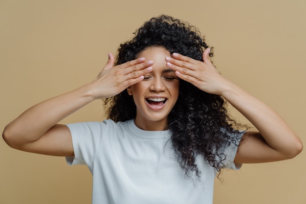 De gelukkige donkere vrouw behandelt ogen en glimlachen terwijl het hebben van pret