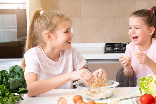 De gelukkige familie grappige jonge geitjes bereiden het deeg voor, bakken koekjes in de keuken. zusters plezier samen lachen