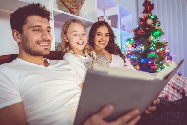 De gelukkige familie lag op het bed en las een verhaaltje bij de kerstboom