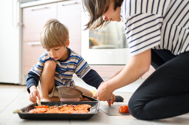 De gelukkige familie maakt thuis voedsel. moeder samen haar vier jaar oude zoon peuter koken pizza in de keuken.