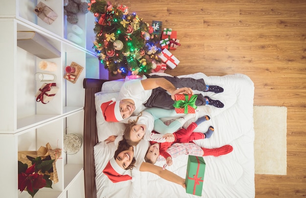 De gelukkige familie zit in een bed met geschenken. uitzicht van boven