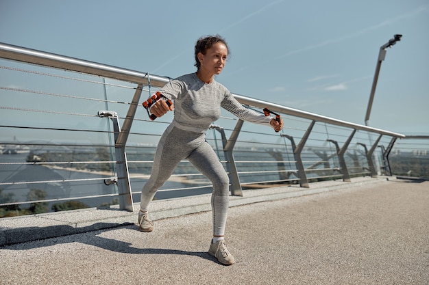 De gelukkige gezonde en sportieve vrouw doet harnasoefeningen in zonnige dag