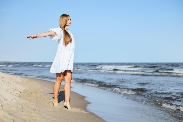 De gelukkige glimlachende mooie vrouw loopt met open armen op het oceaanstrand.