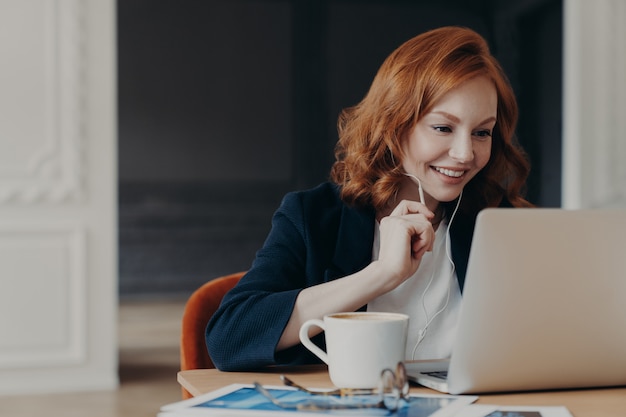 De gelukkige glimlachende vrouwelijke ondernemer heeft online conferentie via moderne laptop computer