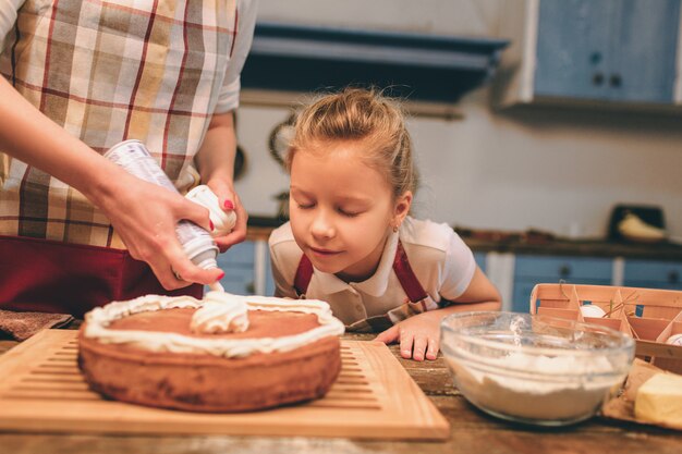 De gelukkige houdende van familie bereidt samen bakkerij voor. Moeder en kinddochtermeisje die pret in de keuken hebben. Trots houden van vers gebakken zelfgemaakte taart. Ze snuiven.