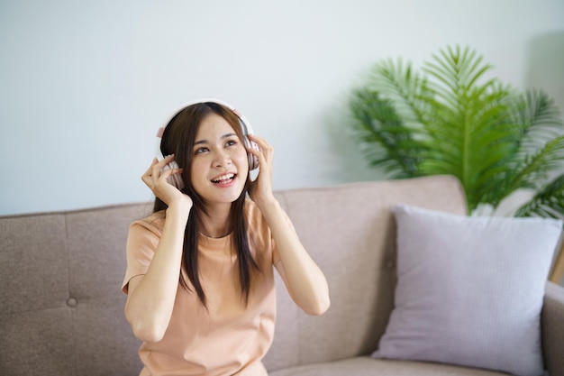 De gelukkige jonge Aziatische vrouw die hoofdtelefoon draagt die aan muziek luistert ontspant in woonkamer