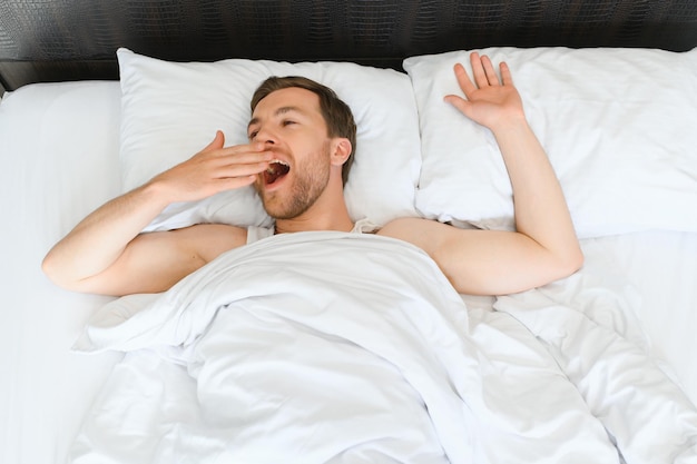 De gelukkige jonge bebaarde man ontspant thuis op bed