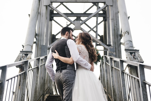 De gelukkige jonge glimlachende bruid en de bruidegom bevinden zich op de hangbrug. trouwfoto's op een interessante plek