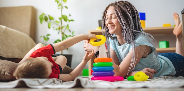 De gelukkige jonge moeder en haar kind verzamelen samen een kleurrijke piramide