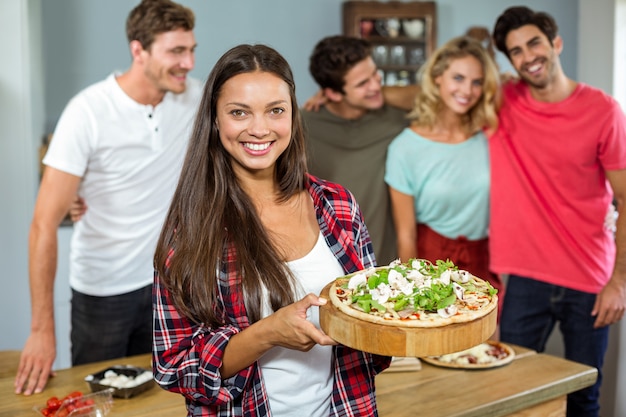 De gelukkige jonge pizza van de vrouwenholding met vrienden thuis