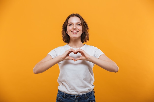 De gelukkige jonge vrouw die opzij kijkt maakt hartgebaar.