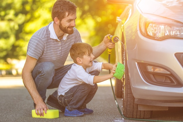 De gelukkige jongen en de vader die een auto buiten wassen