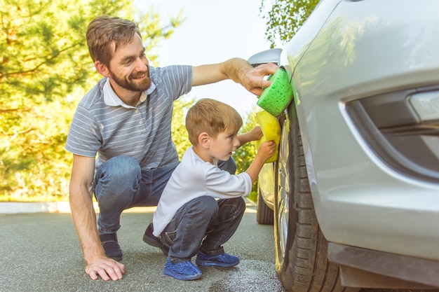 De gelukkige jongen en een vader maken een wiel van een auto schoon