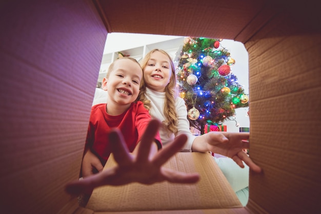 De gelukkige kinderen openen de doos bij de kerstboom