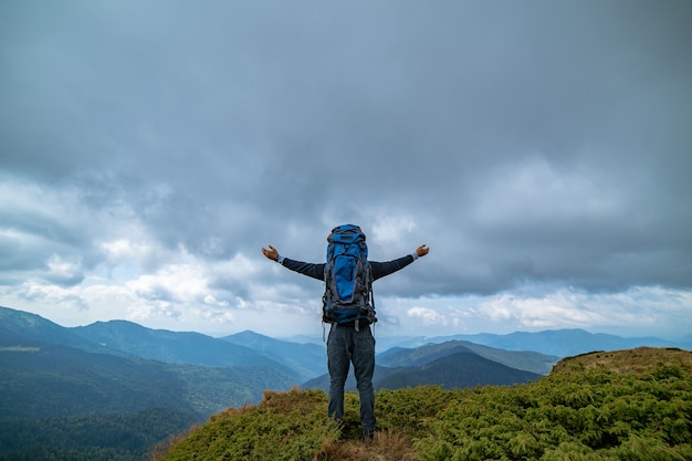 De gelukkige man die op de berg staat op de achtergrond van de regenachtige wolken