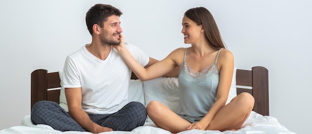 De gelukkige man en een vrouw zitten op het bed op de witte achtergrond