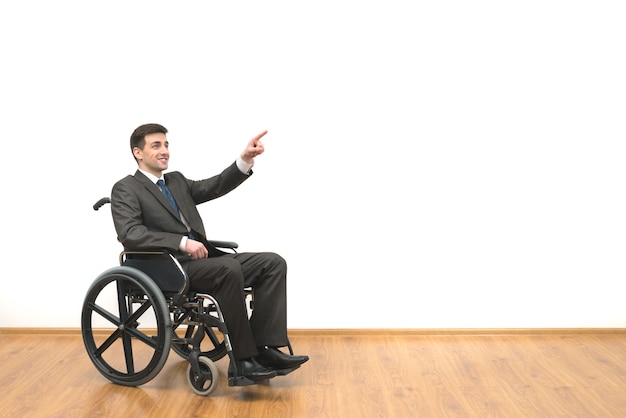 De gelukkige man in een rolstoel gebaren op de witte muur achtergrond