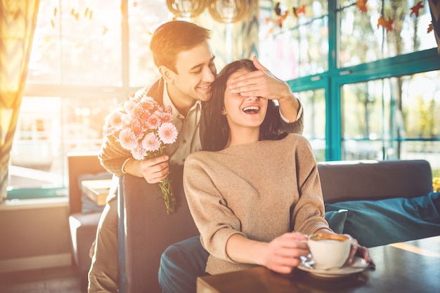 De gelukkige man maakt een verrassing met bloemen voor een vriendin in het restaurant