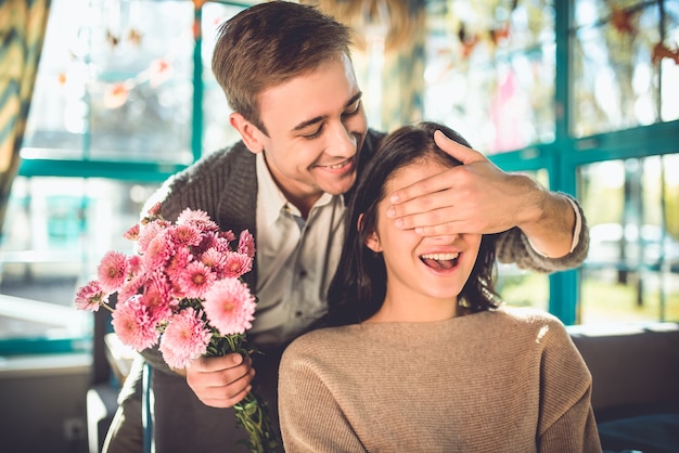 De gelukkige man maakt een verrassing met bloemen voor een vrouw in het restaurant