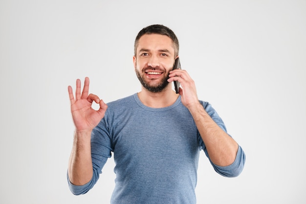 De gelukkige mens maakt ok gebaar sprekend door mobiele telefoon.