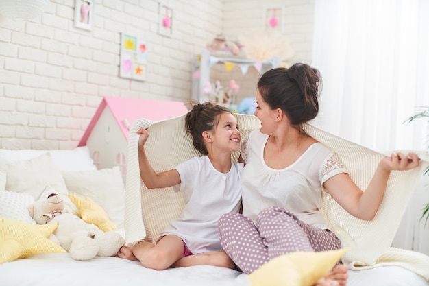 De gelukkige moeder en de dochter omhelzen en bekijken elkaar met liefdezitting op bed.