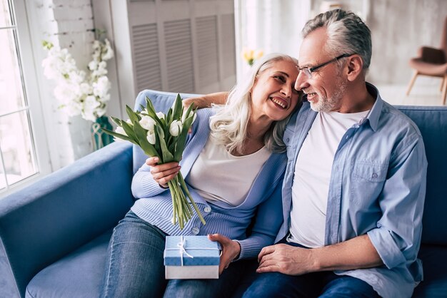 De gelukkige oudere man die een cadeau geeft aan een vrouw met bloemen