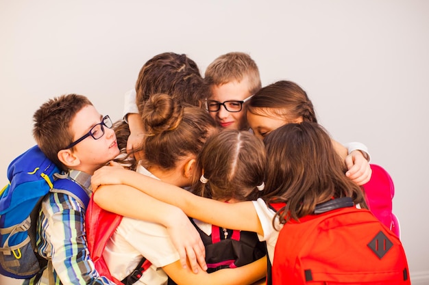 De gelukkige schooljongens en schoolmeisjes knuffelen elkaar op een witte muurachtergrond