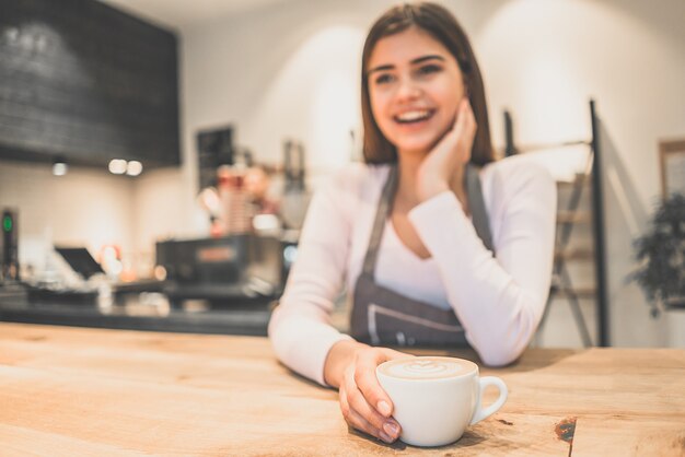 De gelukkige serveerster met een kopje koffie in een café