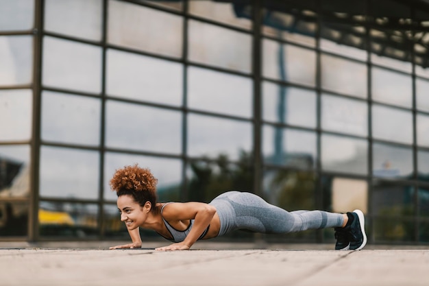 De gelukkige stedelijke sportvrouw doet push-ups op straat