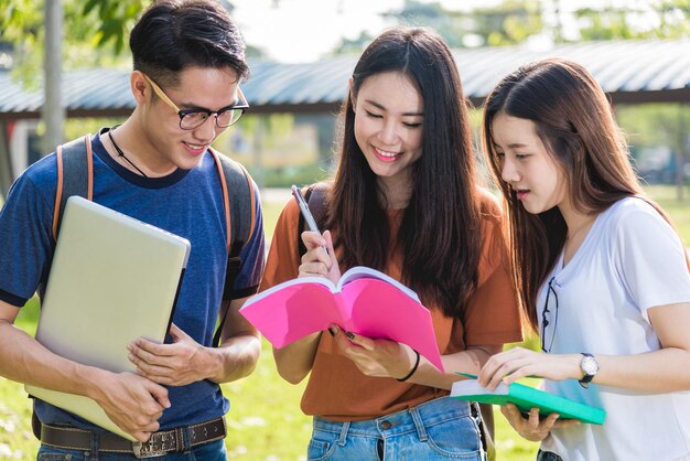 De gelukkige studenten van groepsvrienden die zich op de universiteit bevinden die schoolboek samen lezen