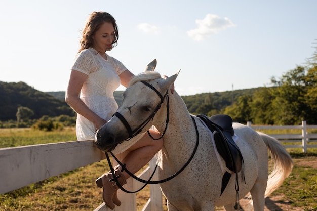 De gelukkige vrouw aait een paard terwijl ze op een hek zit