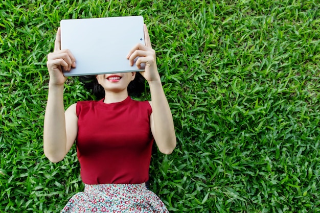 De gelukkige vrouw bepaalt op gras met tablet