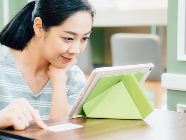 De gelukkige vrouw gebruikt een witte modelcreditcard voor online het winkelen op tablet.