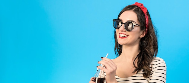 De gelukkige vrouw in zonnebril die een cola drinkt op de blauwe achtergrond