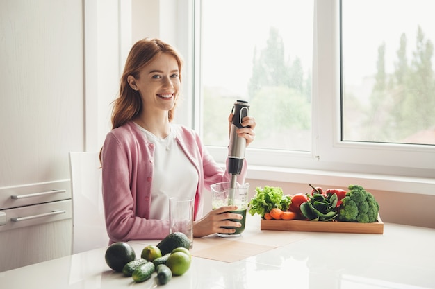 De gelukkige vrouw maakt vers groentesap met behulp van een fruitpers het glimlachen