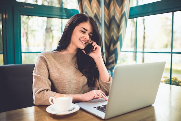 De gelukkige vrouw met een laptoptelefoon in het restaurant