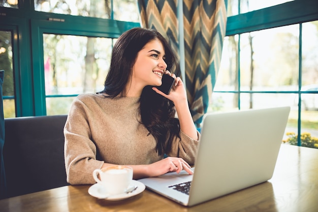 De gelukkige vrouw met een laptoptelefoon in het restaurant