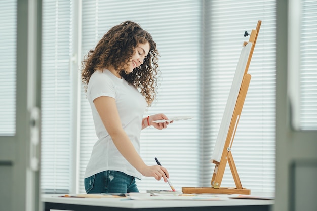 De gelukkige vrouw schildert een schilderij op de ezel