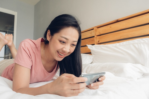 De gelukkige vrouw speelt mobiel spel op haar bed.