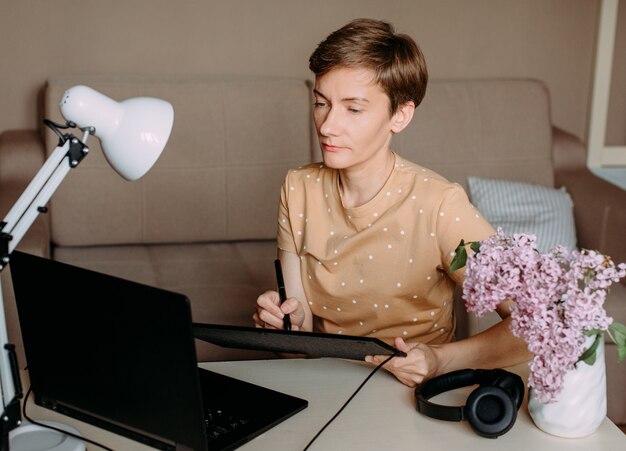 De gelukkige vrouw trekt laptop van het grafische tabletbureau