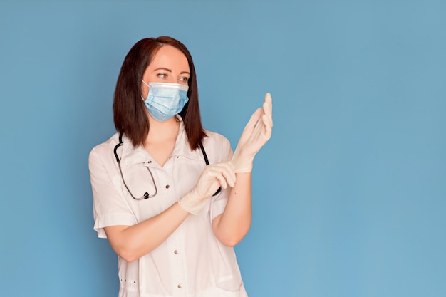 De gelukkige vrouwelijke arts in medisch masker zet medische handschoenen met een stethoscoop aan. Kopieer ruimte