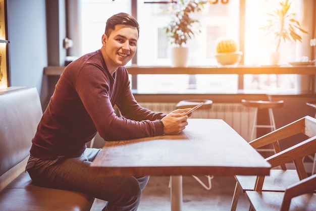 De gelukkige zakenman zit met een tablet in het café