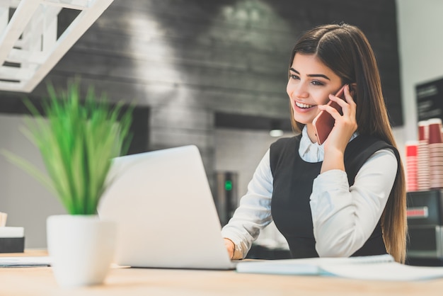 De gelukkige zakenvrouw telefoneert aan de desktop