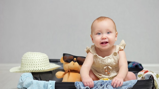 De gelukkige zitting van het babymeisje in koffer glimlacht en lacht