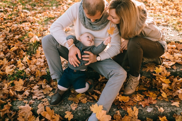De gelukkige zitting van het familiepaar op treden die door de herfstbladeren worden behandeld en hun mooi kind houden